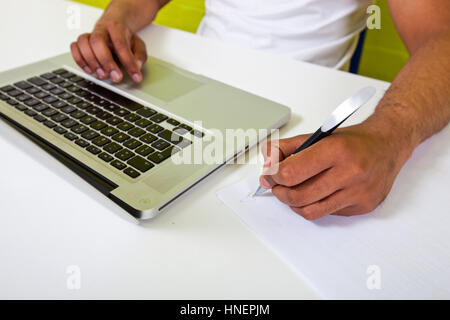 Close up di indiani mans mani scrittura su carta accanto al laptop Foto Stock