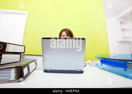 Testa di donna prendendo fuori sopra la parte superiore del computer portatile Foto Stock