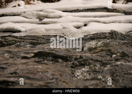 Close up di acqua che attraversa parzialmente congelati creek. Foto Stock