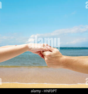 Mani di una giovane coppia tenuti insieme contro un cielo, mare e spiaggia sfondo. Foto Stock