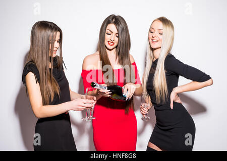 Tre giovani donne che celebra e bevendo champagne sul partito su sfondo bianco Foto Stock
