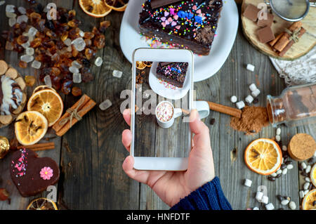 Ragazza fotografata su uno smartphone tabella con bere cioccolata calda con marshmallows e altri dolci Foto Stock