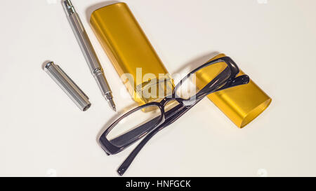 Occhiali neri, oro caso e pen a isolare lo sfondo bianco Foto Stock