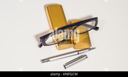 Occhiali neri, oro caso e una penna. Isolare lo sfondo bianco. Foto Stock
