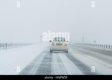 Bianco auto la guida su una strada66 in Inghilterra settentrionale in inverno in tempesta di neve Foto Stock