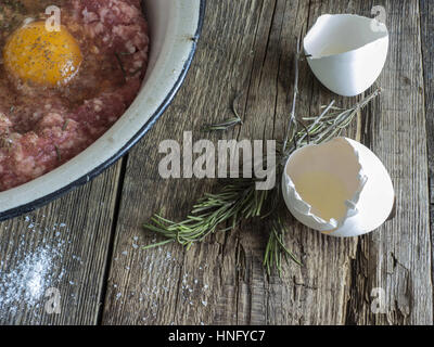 Per la cottura delle costolette. 12 Feb, 2017. Agnello forcemeat nel recipiente metallico, l'uovo, il rosmarino, il mulino di pepe su un vecchio weathered tavolo in legno Credito: Igor Golovniov/ZUMA filo/Alamy Live News Foto Stock