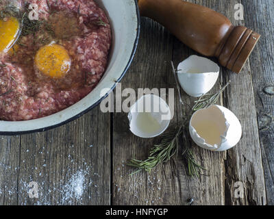 Per la cottura delle costolette. 12 Feb, 2017. Agnello forcemeat nel recipiente metallico, l'uovo, il rosmarino, il mulino di pepe su un vecchio weathered tavolo in legno Credito: Igor Golovniov/ZUMA filo/Alamy Live News Foto Stock