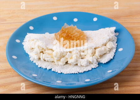 Casabe (ingaggiami, beiju, bob, biju) - flatbread di manioca (tapioca) con ricotta e miele sulla piastra su sfondo di legno. Messa a fuoco selettiva Foto Stock