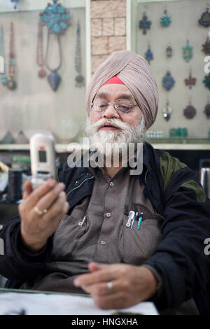 New Delhi, India - Febbraio, 16 2010: l'uomo che gestisce un negozio di posta indesiderata in Delhi ispezione di un telefono cellulare sta considerando l'acquisto. Foto Stock