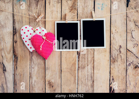 Due cuore e due photo frame appeso sulla corda stendibiancheria con sfondo di legno. Foto Stock