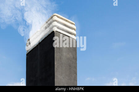 Il fumo aumenta da un camino in inverno giorno contro il cielo blu Foto Stock