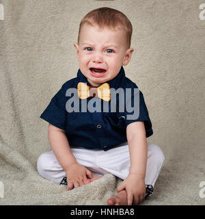 Bambino piangere mentre guardando la telecamera seduta su una coperta Foto Stock