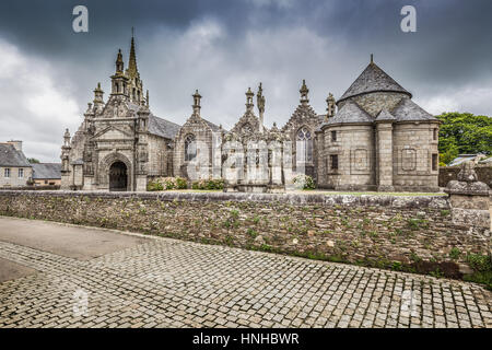 Visualizzazione classica della famosa antica Chiesa Parrocchiale di San Miliau con scure nuvole drammatico in estate nel comune di Guimiliau, Bretagna Francia Foto Stock