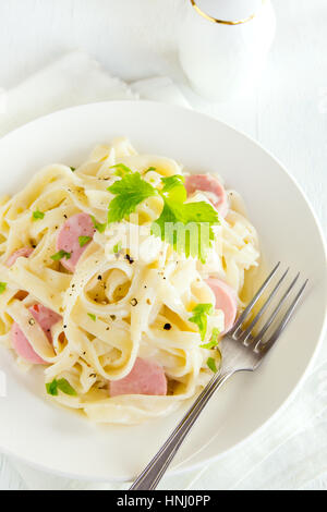 Alfredo tagliatelle con salsicce, salsa cremosa e verdi su piastra bianca - fatti in casa pasta cremosa Foto Stock