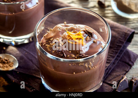 Mousse al cioccolato guarnita con scorza di arancia in bicchieri su sfondo in legno close up - deliziosa casa budino di cioccolato Foto Stock