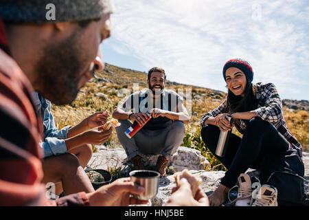 Gruppo di persone rilassarsi e mangiare durante l'escursione. Giovane donna con amici prendendo una pausa durante una passeggiata in campagna. Foto Stock