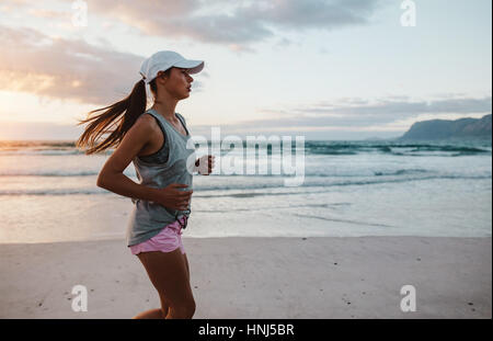 Vista laterale colpo di montare la giovane donna jogging sulla spiaggia di mattina. Bella femmina caucasica su run mattutino lungo la spiaggia. Foto Stock