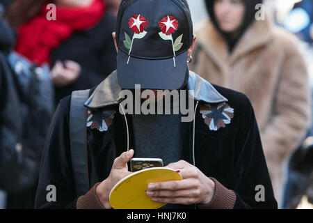 Uomo con cappuccio nero con fiori rossi guardando smartphone prima di N 21 fashion show, la Settimana della Moda Milanese street style on gennaio 16, 2017. Foto Stock