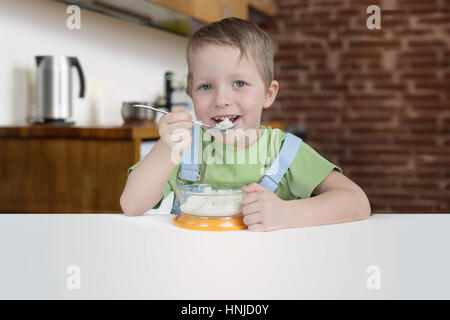 Cinque anni ragazzo mangia il porridge in cucina Foto Stock