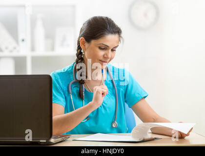 Medico donna scrittura bianco prescrizione seduto alla scrivania in ospedale Foto Stock