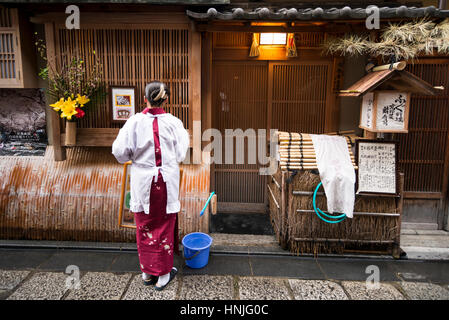 Un lavoratore di sesso femminile che la pulizia entrata del ristorante prima di aprire, quartiere di Gion, Kyoto, Giappone Foto Stock