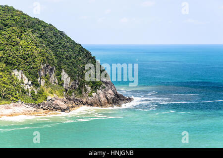 Mare blu sfondo con una montagna accanto ad essa, la vegetazione verde, rocce e mare di colpire le rocce. Foto Stock