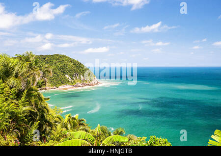 Mare blu sfondo con una montagna accanto ad essa, la vegetazione verde, rocce e mare di colpire le rocce. Spiaggia di Pernambuco, costa di Guarujá. Foto Stock