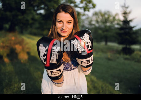 Giovani caucasici boxer femmina nero indossa guantoni da pugilato, sorridente verso la telecamera Foto Stock