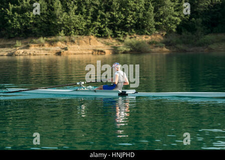 Un giovane singolo scull concorrente a remi pagaie sul tranquillo lago Foto Stock