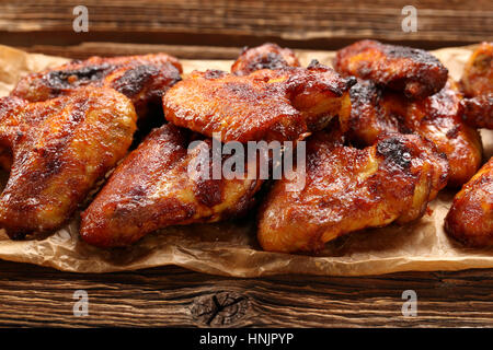 Ali di pollo cotto al forno in un tegame su sfondo di legno Foto Stock