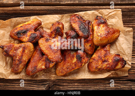 Ali di pollo cotto al forno in un tegame su sfondo di legno Foto Stock