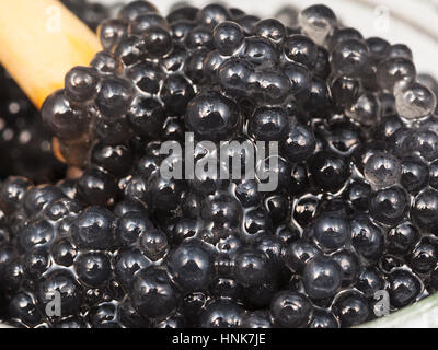 Colorati di nero decapato caviale di halibut pesce con il cucchiaio di legno vicino fino in un barattolo di vetro Foto Stock