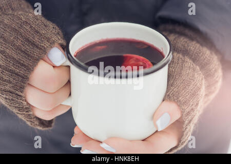 Donna che mantiene rustico bianco tazza di vin brulé con spezie e agrumi nelle sue mani all'aperto in inverno freddo giorno, close up Foto Stock