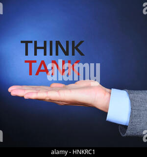 La mano di un giovane uomo caucasico indossando un abito grigio e il testo think tank su uno sfondo nero alleggerito in blu Foto Stock