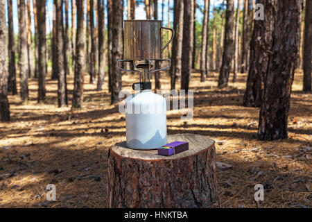 Nella foresta sul moncone elementi si trovano un bruciatore a gas con una tazza di partite di caccia Foto Stock