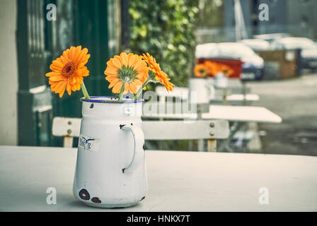 Orange Gerbera daisy fiori in una brocca in metallo su un tavolo del bar esterno Foto Stock