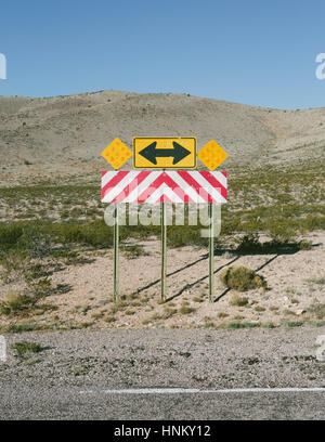 Freccia direzionale e il simbolo di attenzione lungo rurale strada nel deserto Foto Stock