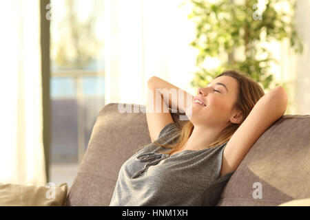 Ritratto di una ragazza rilassante su un divano dopo il lavoro a casa seduto su un divano nel soggiorno di casa con una calda luce del tramonto Foto Stock