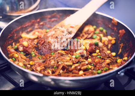 La cottura della pasta salsa con una spatola di legno in una casseruola sul fornello Foto Stock