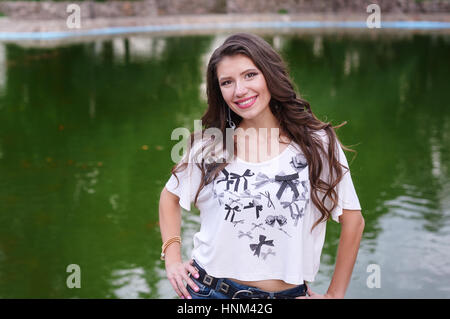 Sorridente giovane donna in piedi sullo sfondo del lago nel parco Foto Stock