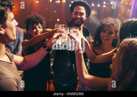 Gruppo di amici avente le bevande presso il night club party. I giovani godono presso un bar cocktail di tostatura. Foto Stock