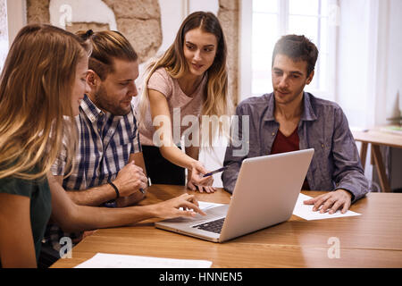 Young business team con due maschio e femmina di due professionisti in una presentazione interattiva di incontro con un pc laptop sulla scrivania tra di essi Foto Stock