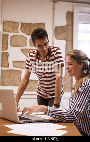 Professional giovane imprenditrice che mostra un giovane uomo qualcosa su un laptop stanno condividendo mentre si sta guardando il suo Foto Stock