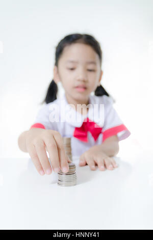 Asian bambina in Thai studente uniforme delle monete di impilamento, selezionare la messa a fuoco a portata di mano leggera profondità di campo Foto Stock