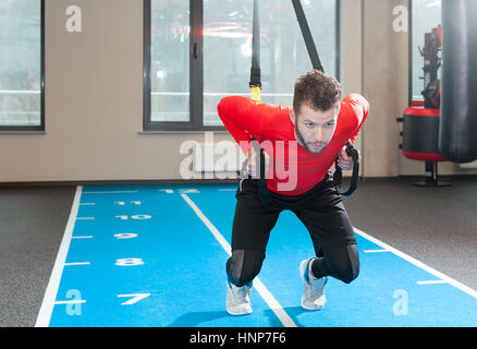 Ricci bianco barbuto uomo sportivo esercitando con cinghie di fitness in palestra Foto Stock