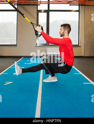 Ricci bianco barbuto uomo sportivo esercitando con cinghie di fitness in palestra Foto Stock