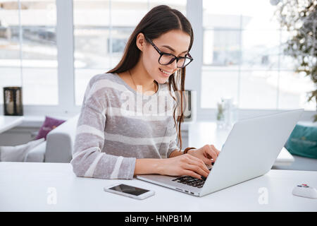 Immagine della giovane e bella signora con gli occhiali in seduta cafè al freddo inverno giorno e tramite computer portatile. Foto Stock
