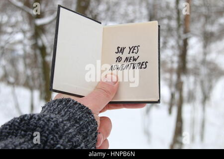 Mano che tiene un libro con la scritta dire sì a nuove avventure sullo sfondo della foresta di inverno Foto Stock