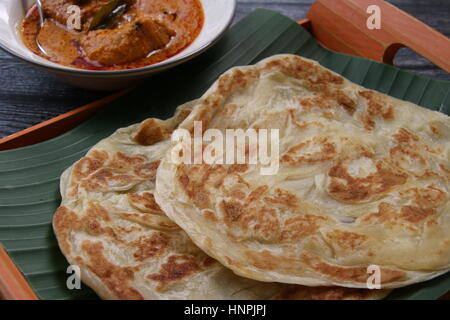 Roti Prata. Indiano-influenzato flatbread. Placcato su una banana-leaf foderato di vassoio di bambù con il pollo al curry serviti separatamente su un vaso di ceramica. Foto Stock