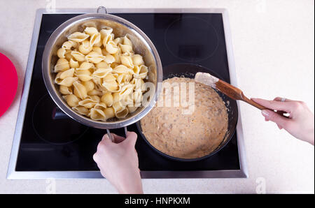 La ragazza si prepara la pasta con la salsa sul fornello ad induzione. Foto Stock